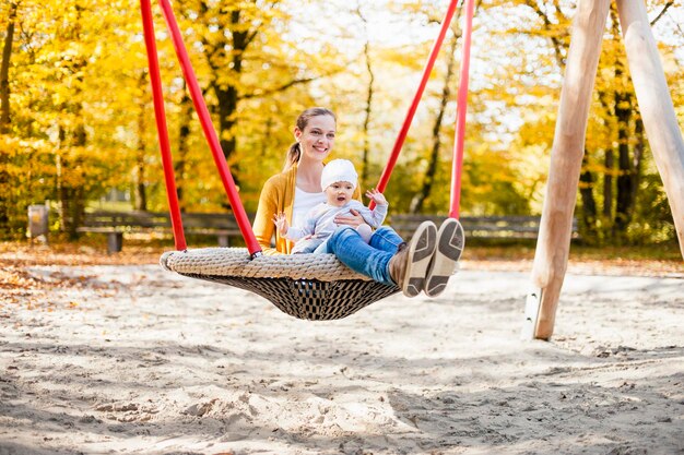 Baby girl sitting with her mother on a swing in autumn