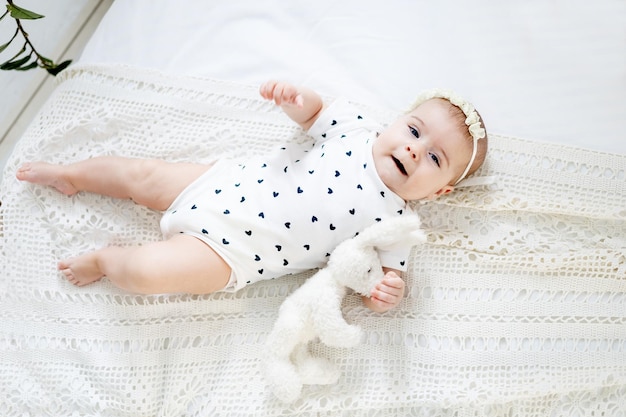 A baby girl of six months on the bed at home playing with a soft toy and her legs a smiling little child with a toy in her hands on the bed in the bedroom