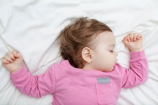 Baby girl sleeping on a white bed, arms raised up