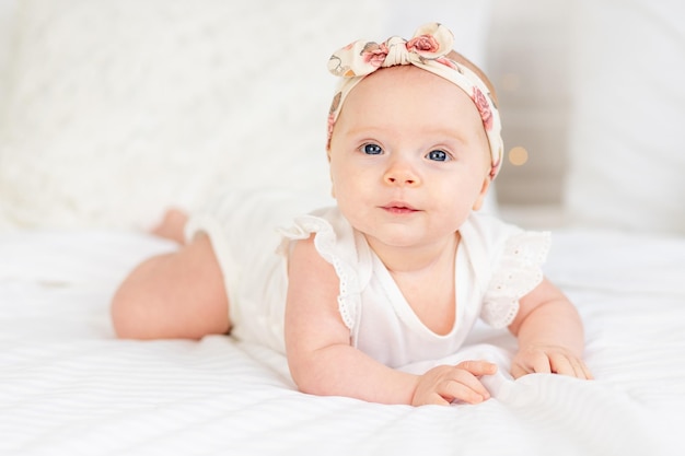 Baby girl smiles lying on her stomach on a white cotton bed at home