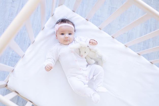 Baby girl smiling on the bed on a white cotton bed with a toy falling asleep or waking up in the morning cute little baby at home