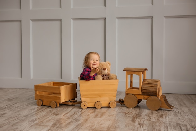 Bambina sorridente in possesso di un orsacchiotto, seduto in una locomotiva in legno giocattolo