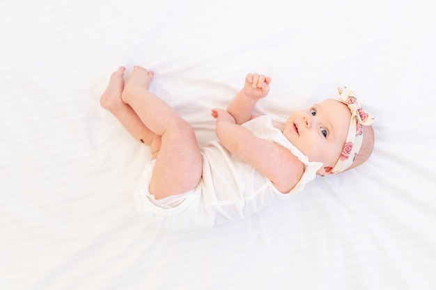 Bambina sorridente sdraiata su un letto di cotone bianco a casa sulla schiena