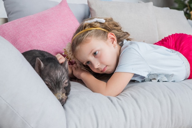 baby girl on sofa near a black vietnamese piglet