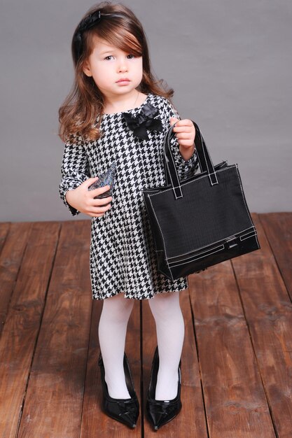 Baby girl standing on wooden floor over gray Wearing stylish dress