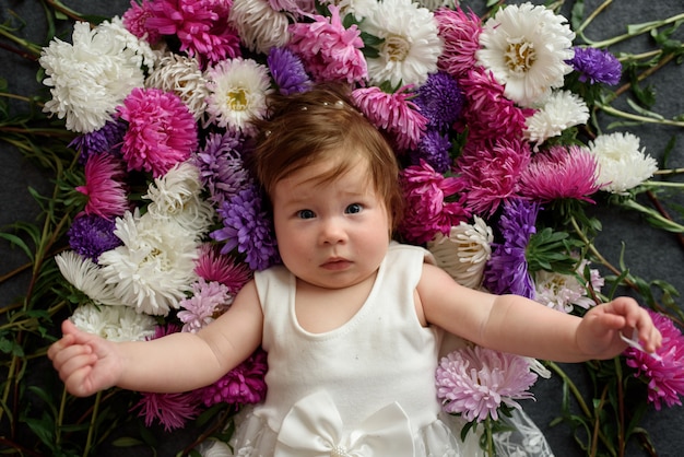 Baby girl in white dress playing with bunch of flowers