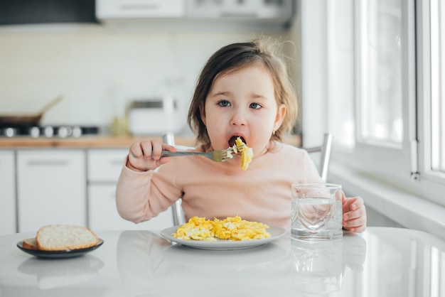 Baby girl in the white pink sweater eating an omelet