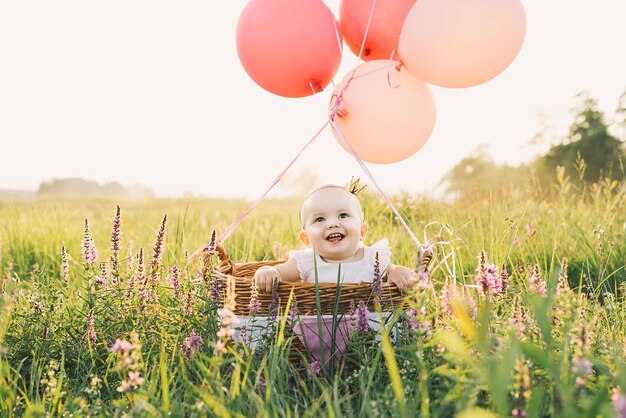 Photo baby girl in wicker basket with pink balloons in sunlight at summertime happy child on nature first birthday party family celebrates one year old baby outdoors photo of childhood dreams holidays