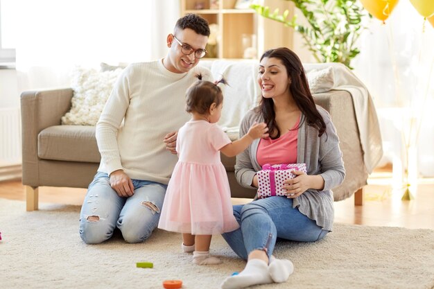 baby girl with birthday gift and parents at home