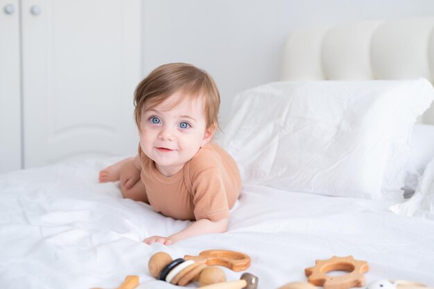 ベッドの上の白い寝具で木のおもちゃで遊ぶ茶色のボディースーツの青い目をした女の赤ちゃん