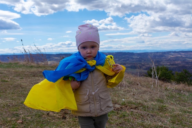 Девочка с флагом Украины на фоне холмов, украинской природы и голубого облачного неба Портрет патриотичной девочки с флагом Украины