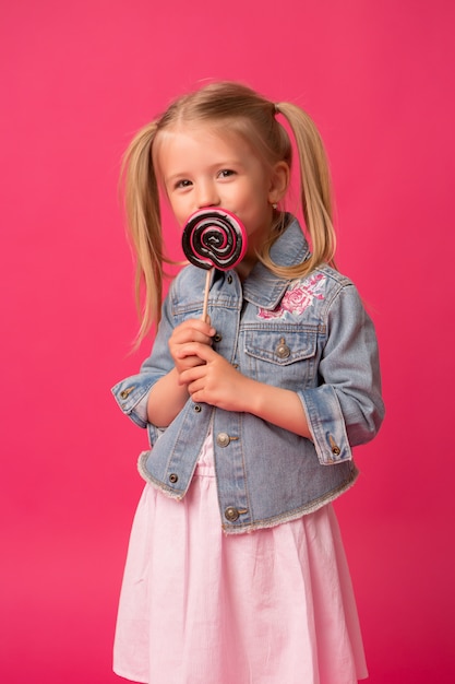 Baby girl with lollipop on pink background