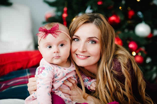 Baby girl with mom on bed near Christmas tree