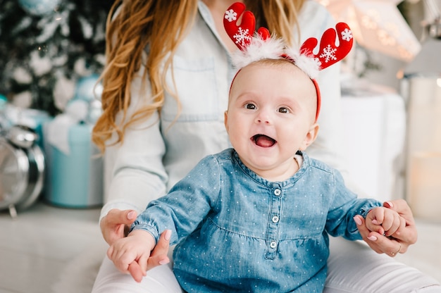 Baby girl with mom on floor near Christmas tree The concept of a family holiday