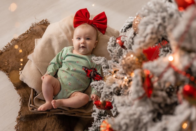 Baby girl with a red bow on her head sits in a christmas tree