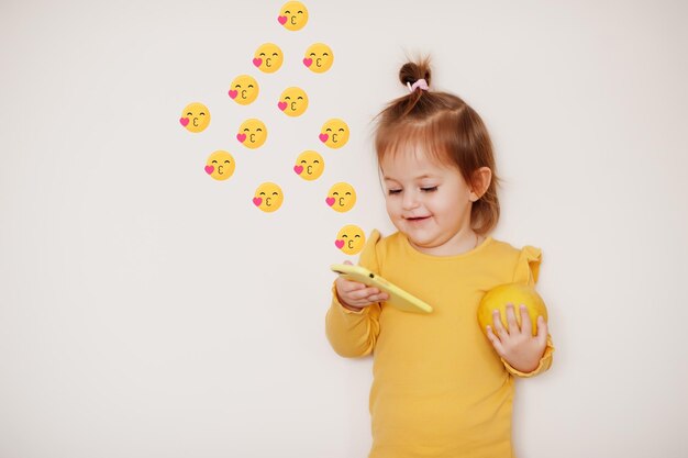 Baby girl in yellow with lemon and mobile phone with kiss emoji, isolated background.