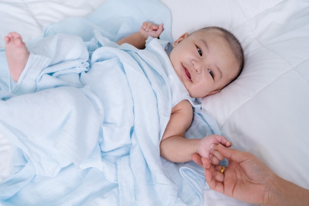 Baby hand holding finger of mother on bed