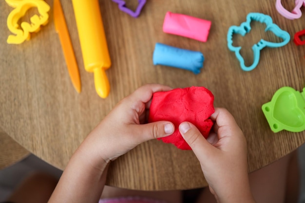 Baby hands holding and kneading red modeling clay on white table background Closeup Toddler development Preparing material for making different colorful shapes