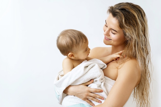 Baby hygiene and care. Young and happy mother and her cute infant son after bathing.