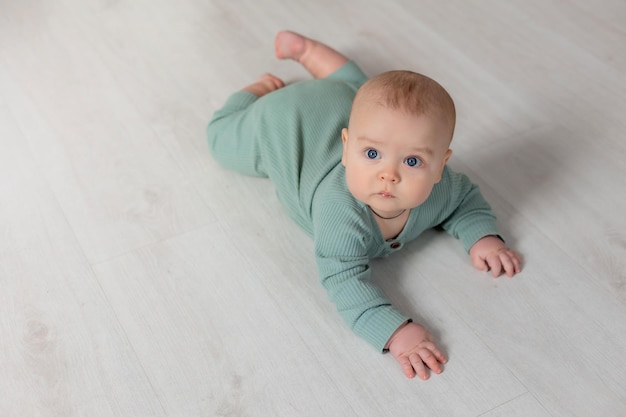 baby in een groene katoenen jumpsuit leert op de grond kruipen kind ontwikkelingsplaats voor tekst