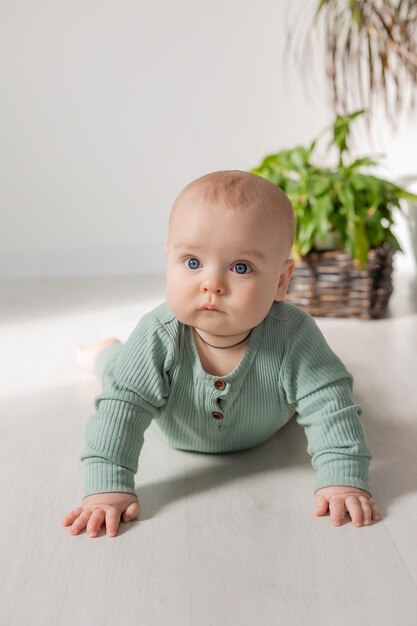 baby in een groene katoenen jumpsuit leert op de grond kruipen kind ontwikkelingsplaats voor tekst