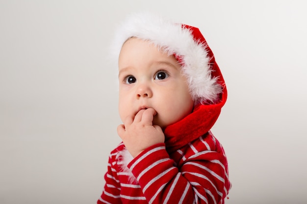 baby in een rode Romper en kerstmuts op een witte muur