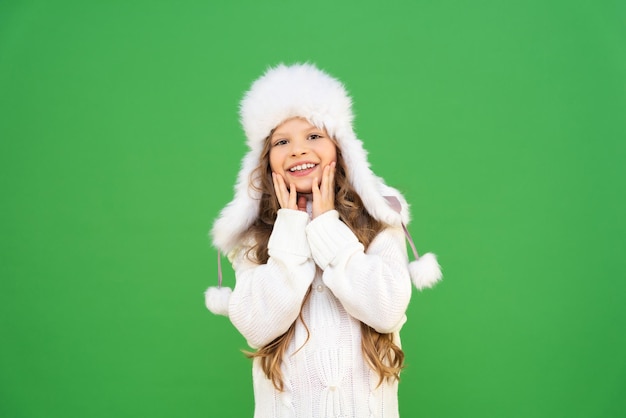 Baby in een trui en een wintermuts legde glimlachend haar handen in haar wangen. Kind in warme winterkleren met lang krullend haar.