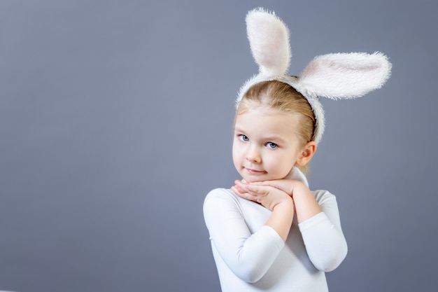 Baby in een wit konijnenkostuum. Leuk meisje met oren van een haas, dichtbij exemplaarruimte.