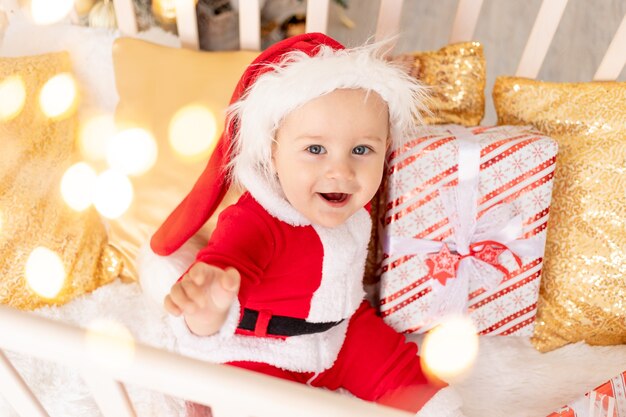 Baby in santa kostuum zitten in wieg thuis met geschenken, nieuwjaar en kerstmis concept