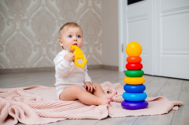 baby in witte kleren zittend op de vloer op een gebreide deken en spelen met educatief speelgoed