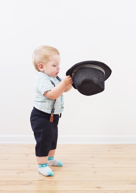 Baby in zwarte hoed, shirt en korte broek met bretels thuis