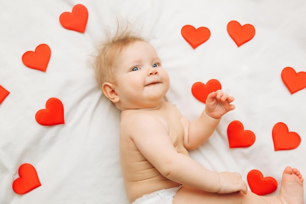 Photo the baby is 6 months old lying on the bed among hearts the concept of love and valentine's day