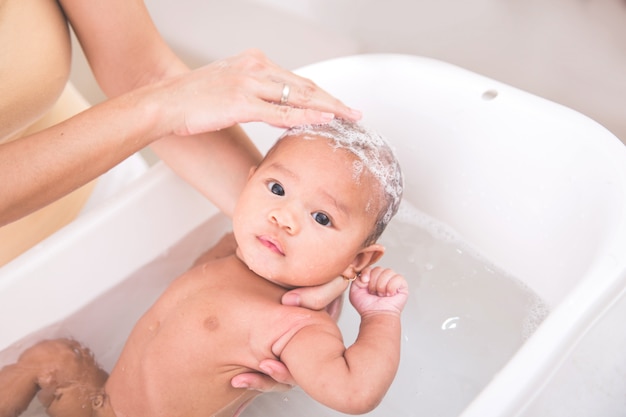 赤ちゃんが母親に水浴びされ、シャンプーされている