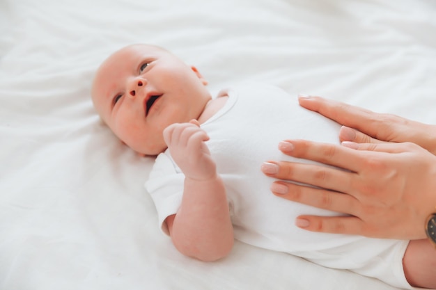 The baby is lying on the bed for 2 months the mother's hand on the baby's stomach newborn baby