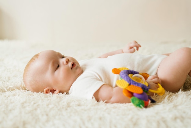 Baby is lying on the bed resting and holding a bright toy in his hands