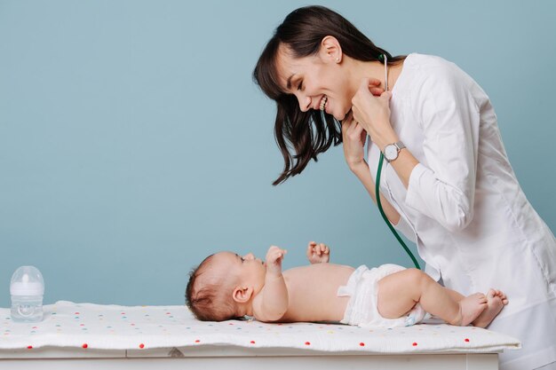 The baby is lying on the table and the pediatrician doctor communicates and plays with him