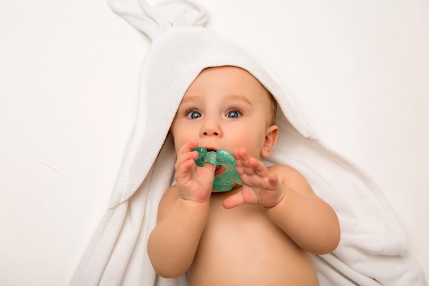 Baby is lying with a teether in a white towel after bathing