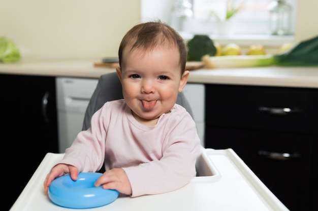 The baby is sitting at the children's chair and waiting for her mother to feed her. 