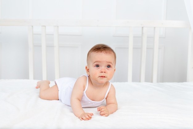 The baby is sitting in a crib in a bright room