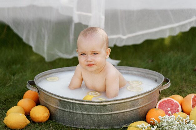 Photo the baby is sitting in a tub on the grass in the yard