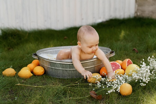 아기가 마당의 풀밭에 있는 욕조에 앉아 있다