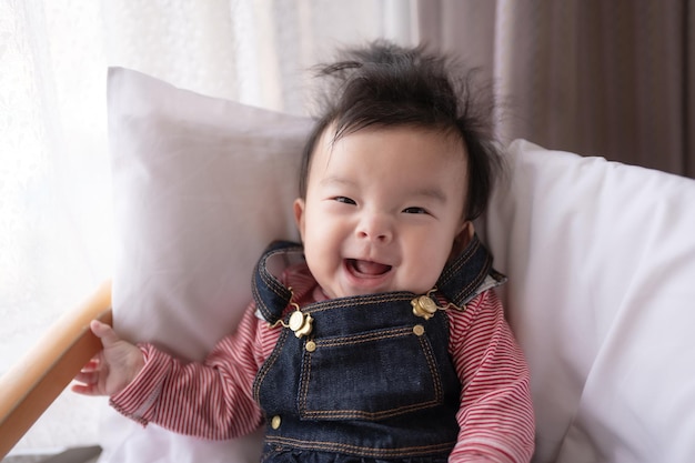 A baby is smiling and is wearing a denim overalls with the word'baby'on it.