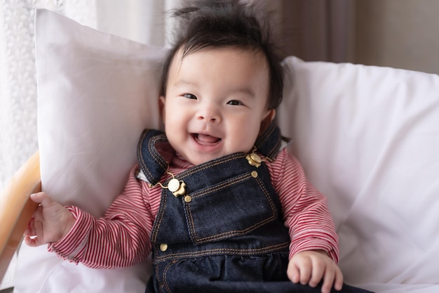 A baby is smiling and wearing overalls and a red striped shirt.