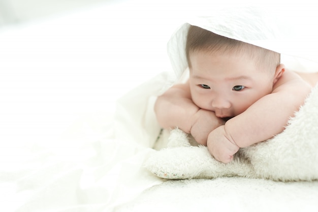 The baby is staring at the front on a white bed with a white background.