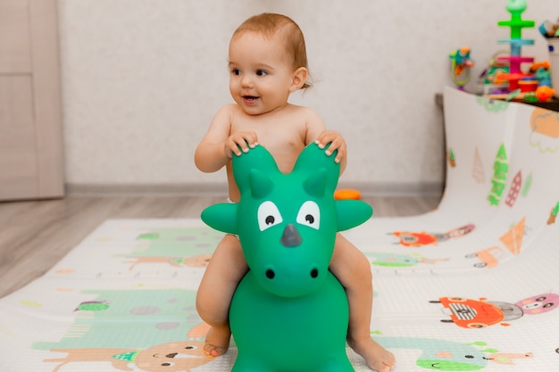 The baby is swinging on a gurney in the shape of a dragon in his room. toy dragon.