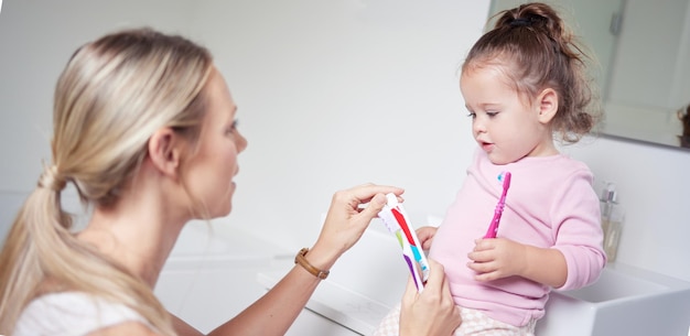 Baby kid brushing teeth with mom in bathroom morning oral hygiene and clean dental healthcare wellness Parent with toothpaste and toothbrush teaching young toddler girl child healthy mouth cleaning