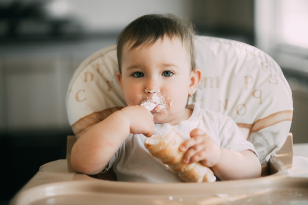 バニラクリームで満たされたおいしいクリームホーンを熱心に食べているキッチンの赤ちゃん