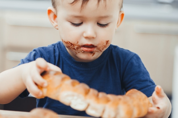 Bambino in cucina che mangia un grosso panino o una torta al cioccolato