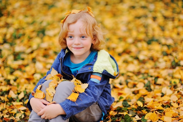 Baby - kleine jongen die met krullend blond haar tegen gele de herfstbladeren glimlacht in het Park