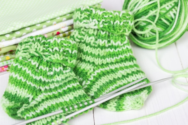 Baby knitting socks on a white wooden background